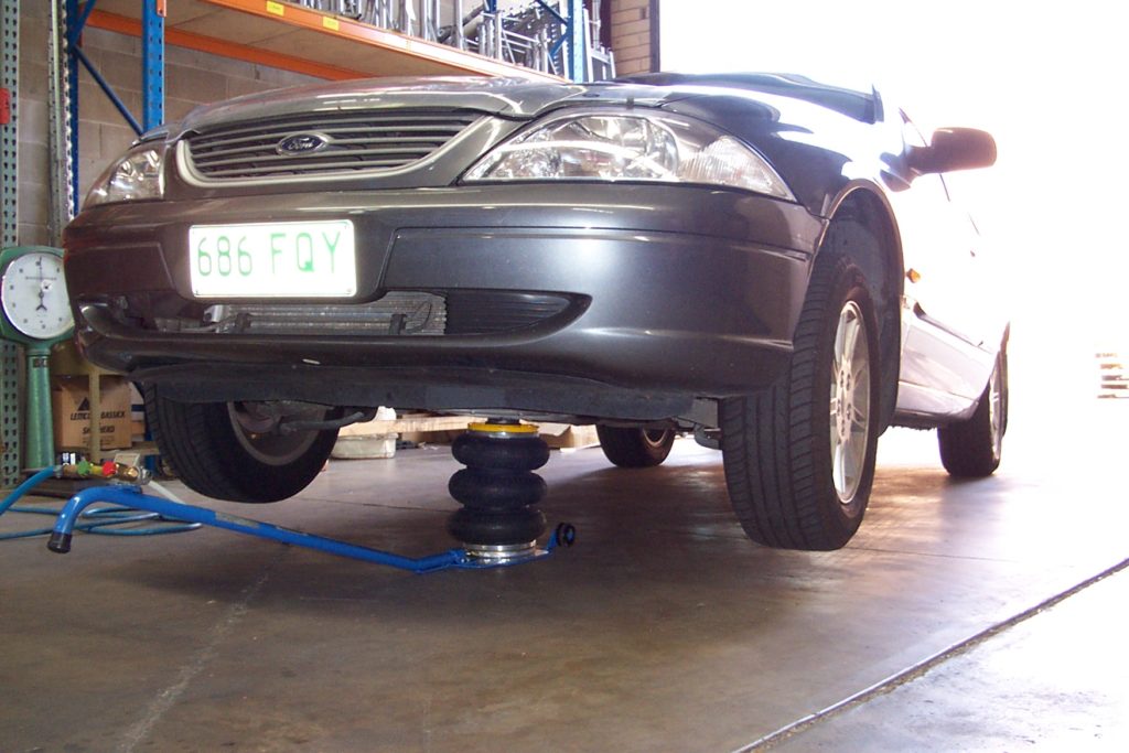 A three bellow Selson Air Jack with a handle, inflated and lifting up the front of a dark-grey Ford car.