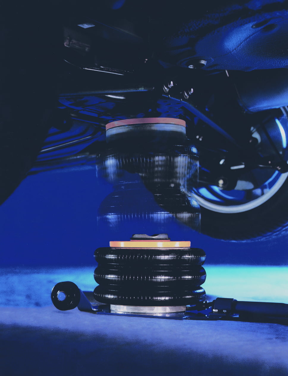 Low-angle view of a pneumatic Selson Air Jack lifting a vehicle under blue lighting, showing the rubber airbag and vehicle suspension system.